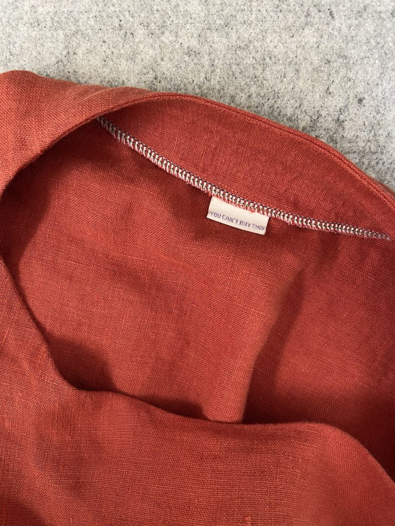 Red linen shirt with collar tag that reads "You can't buy this" in sparkly lavender font.